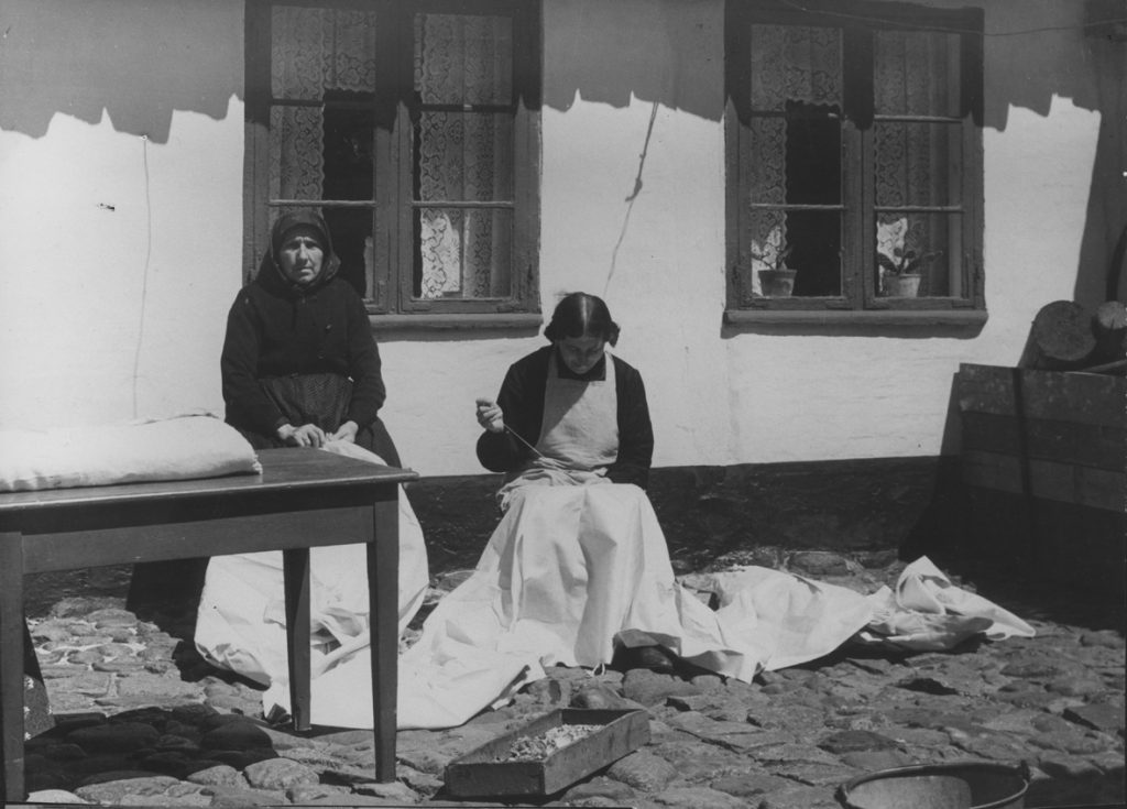 Nelly Jansen (siddende) syr stropper i klæde, før det kan lægges ud til blegning på strandengen. Foto i Dansk Folkemuseum, 1935.